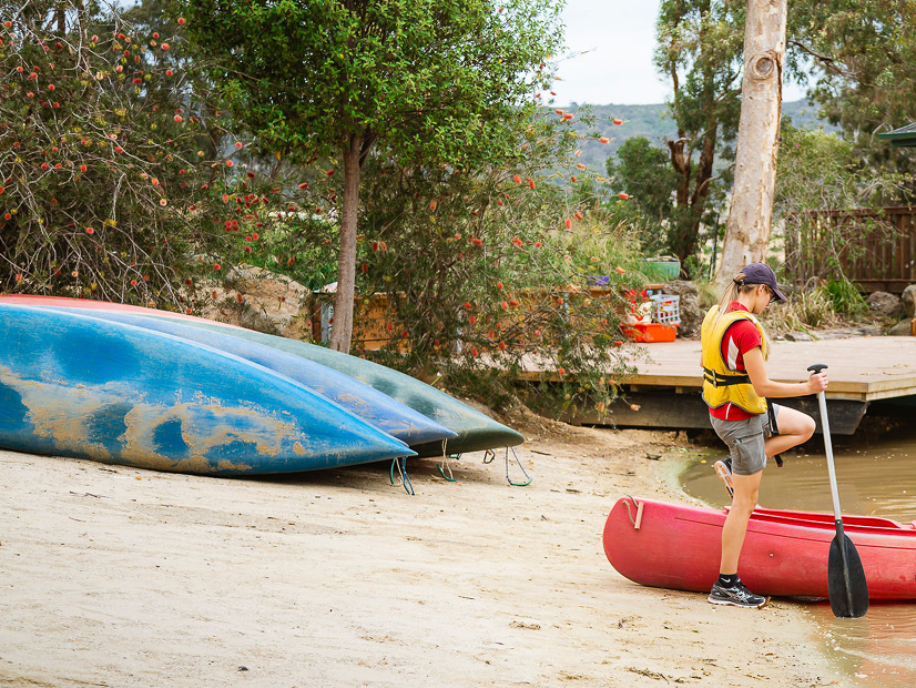 A YMCA staff member stands next to a canoe on the shore of a dam.